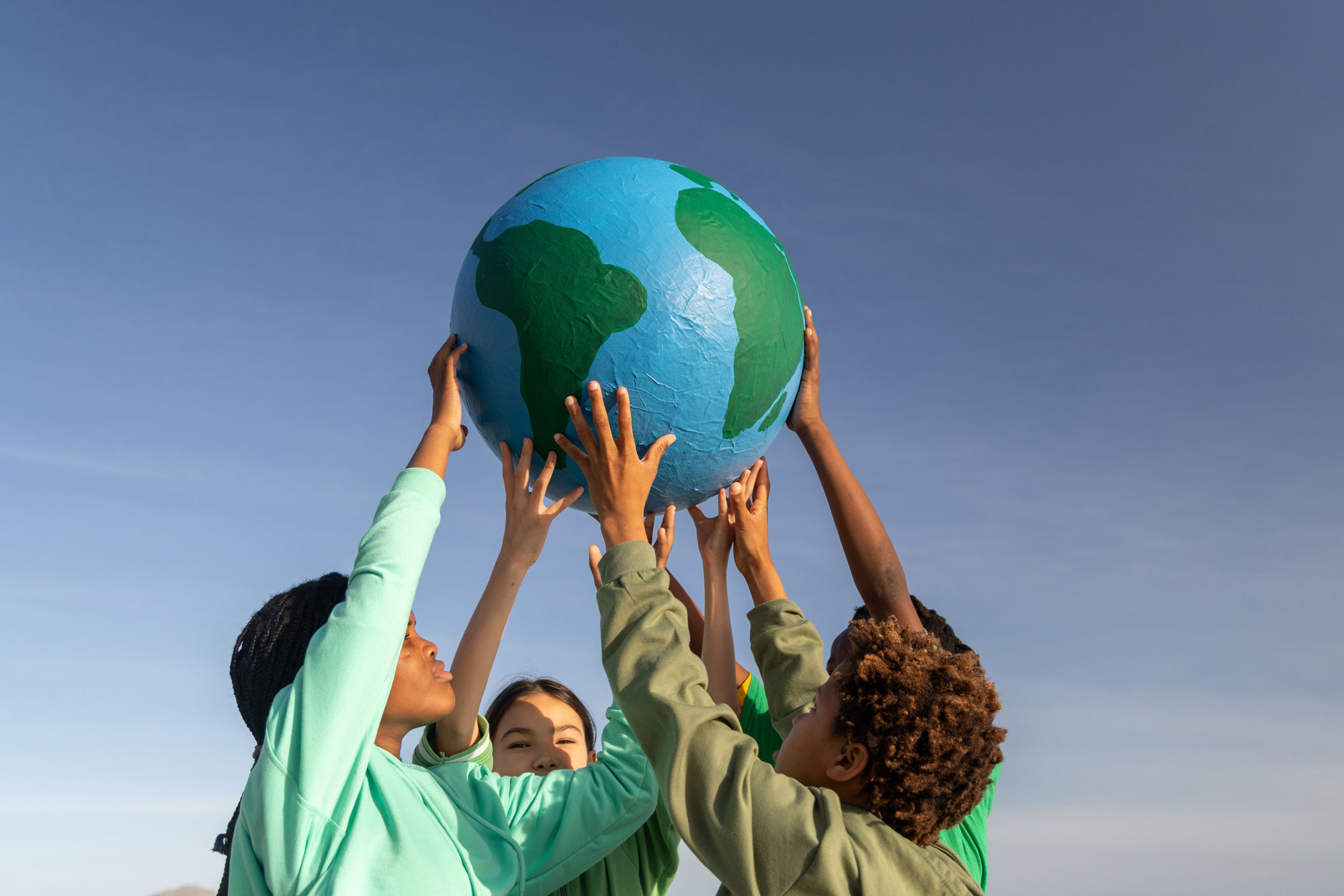 Children holding up a globe with their hands, symbolizing unity and global awareness.