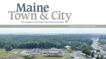Maine Town and City Magazine Cover Volume 85 Issue 9. Ariel Shot of small town in Maine nestled with a wooded area.
