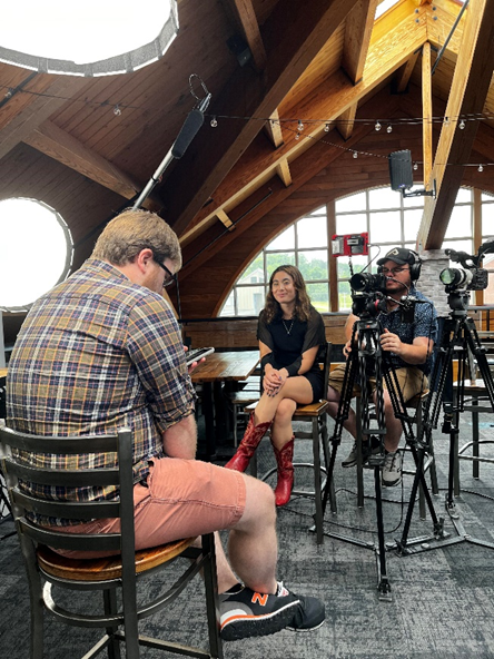 Intern Ava Shapiro sits next to a cameraman, filming a guest.