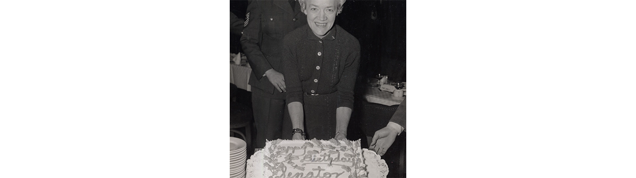 Black and white photo of Margaret Chase Smith posing in front of a birthday cake.