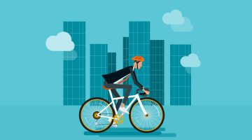 Illustration of a businessperson riding a bicycle through a cityscape, wearing a helmet and suit, with tall glass buildings and clouds in the background. Represents sustainable commuting for National Bike to Work Day.