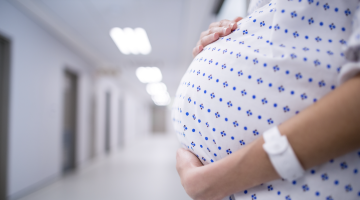 Mid section of pregnant woman standing in corridor.