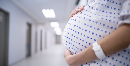 Mid section of pregnant woman standing in corridor.